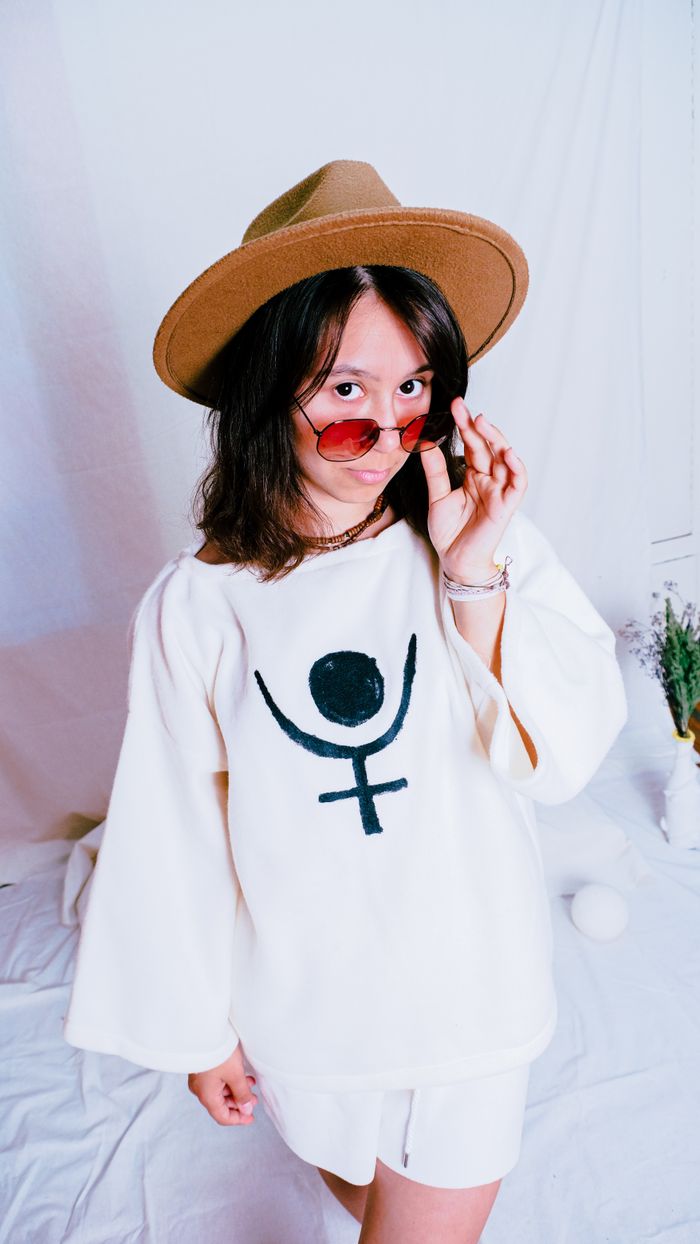 Fashionable woman wearing a hat and red sunglasses poses confidently indoors.