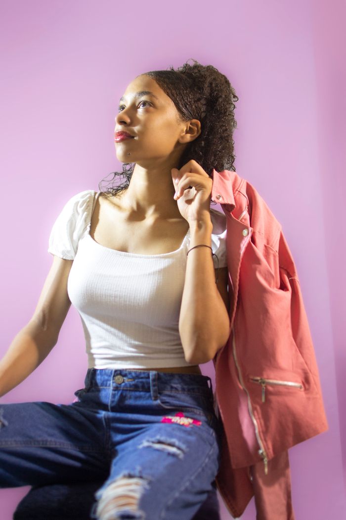Portrait of a woman in jeans and a tank top with a pink jacket. Modern, casual style.
