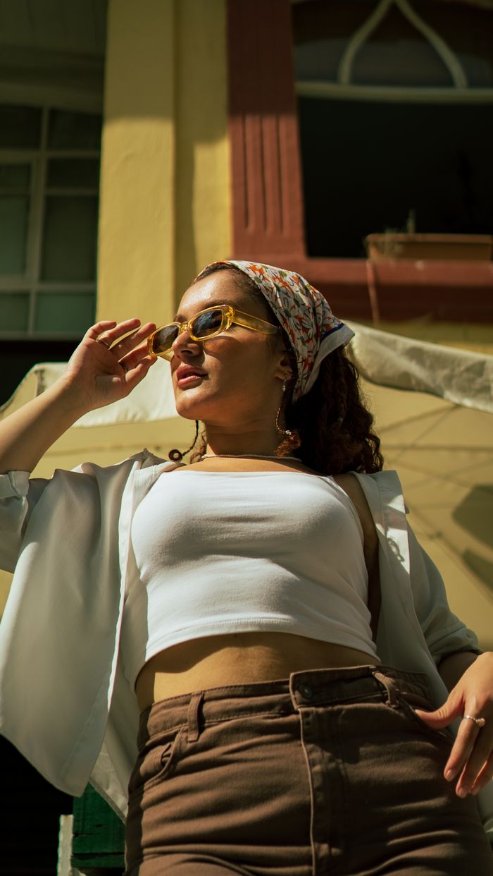 contact-img Young woman in sunglasses and headscarf striking a pose under the sunny sky.