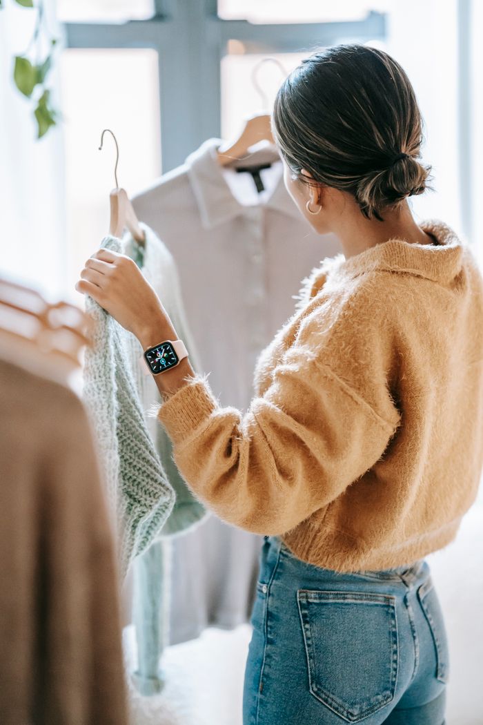our-experience Back view of unrecognizable dark haired female in jeans choosing clothes near rack